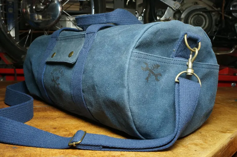 Blue duffle bag on a workbench, motorcycles in the background.