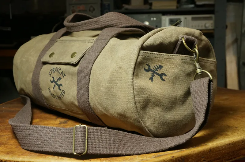 Desert Tan duffle bag with screen-printed logo and shoulder strap on a workbench in the workshop.