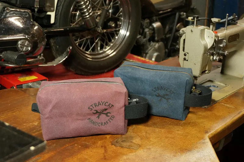 Kulturbeutel in Dusty Rose und Denim Blue vor Motorrädern.