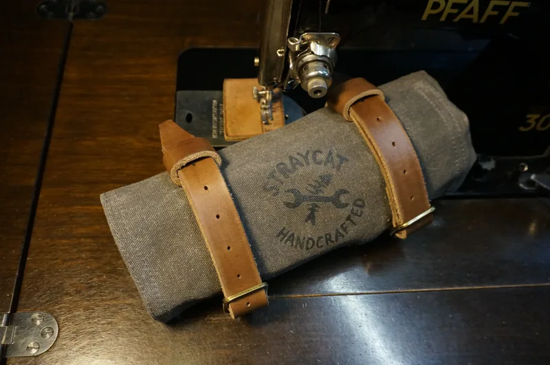 Tool Roll „Nine Lives“ in Storm Grey, rolled up, with light leather straps in front of a Pfaff sewing machine.