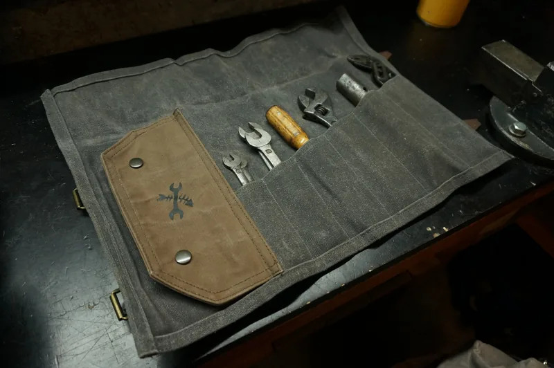 Unrolled Tool Roll „Nine Lives“ in Storm Grey with a brown flap, filled with tools.
