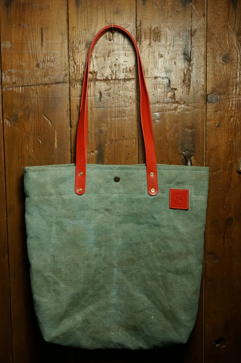 Tent Blue tote bag with red handles and red leather patch, hanging against a wooden wall.
