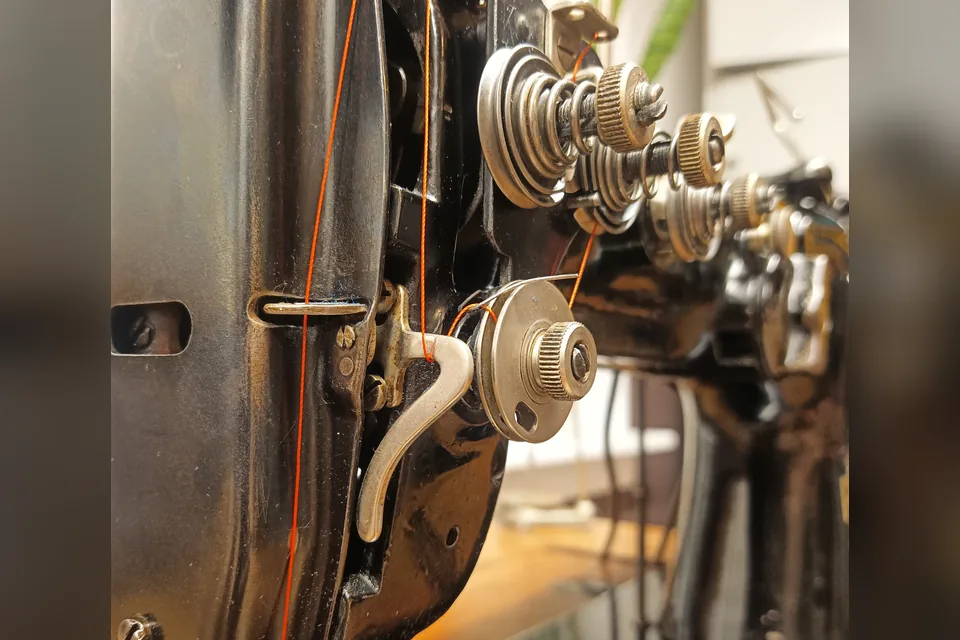 Sewing machine from the side, close-up of the thread tension with orange thread.